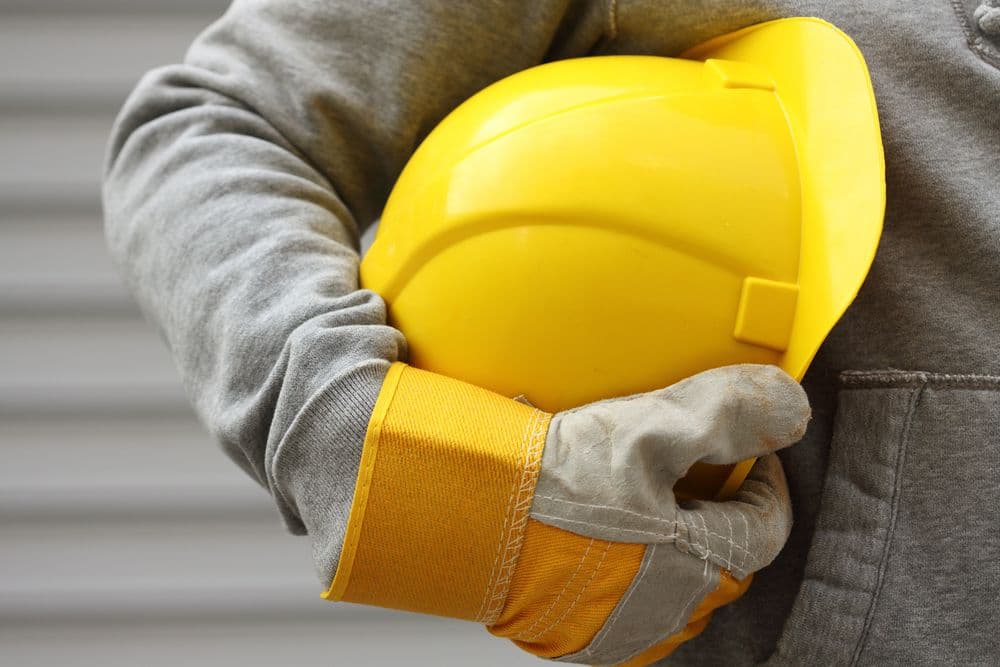 a construction worker wearing a grey sweatshirt, holding their yellow hardhat